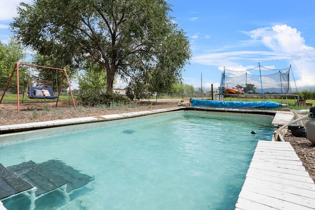 outdoor pool with a playground, a trampoline, and fence