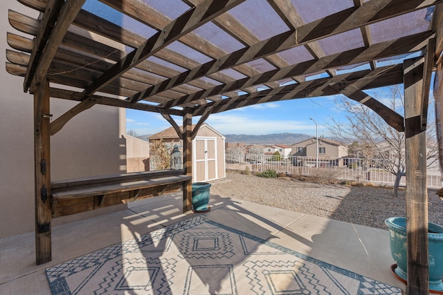 view of patio / terrace featuring fence, a storage unit, an outbuilding, a mountain view, and a pergola