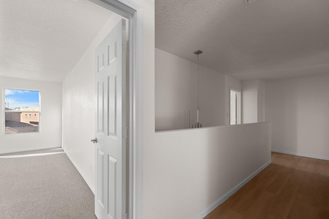 hall with an upstairs landing, baseboards, and a textured ceiling