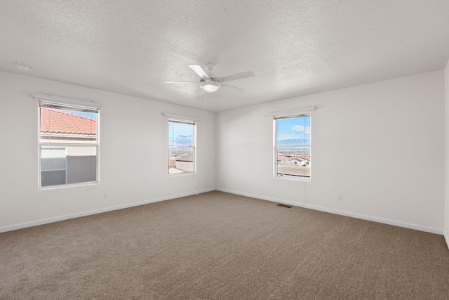 carpeted spare room with a healthy amount of sunlight, a textured ceiling, baseboards, and a ceiling fan