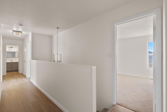 hall with carpet, baseboards, an upstairs landing, a textured ceiling, and a sink