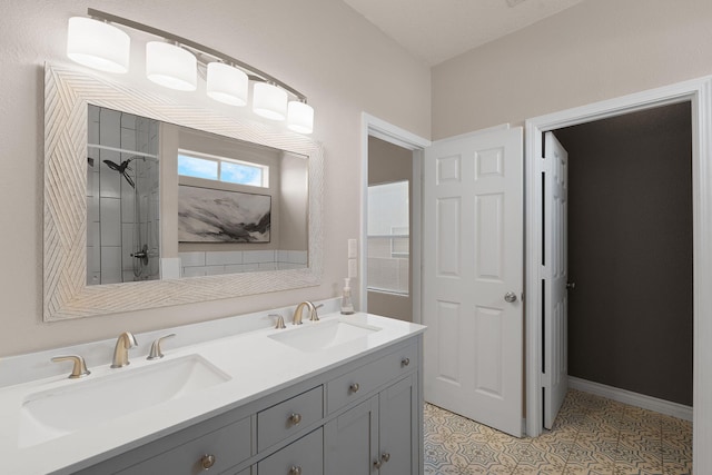 bathroom with a sink, baseboards, double vanity, and a tile shower