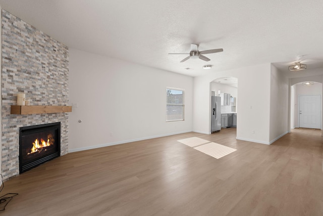 unfurnished living room featuring arched walkways, light wood finished floors, a large fireplace, and ceiling fan