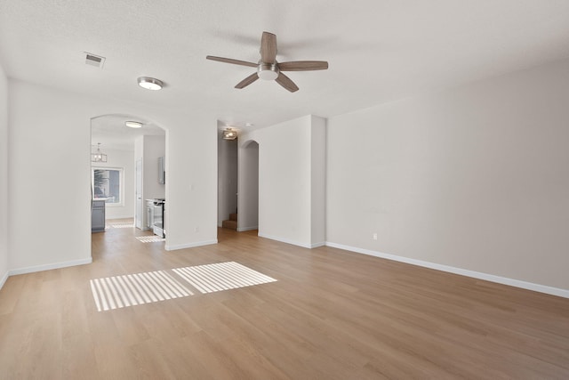 spare room with a ceiling fan, visible vents, baseboards, arched walkways, and light wood-style floors