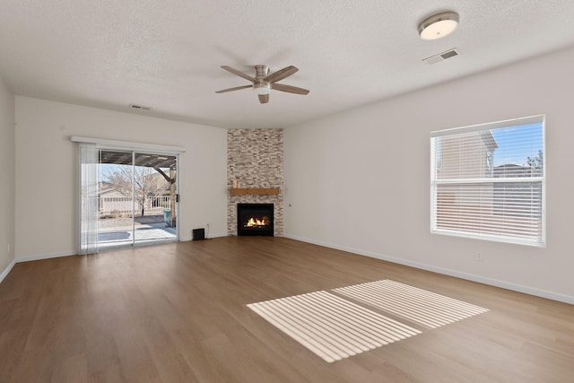 unfurnished living room featuring visible vents, a stone fireplace, and wood finished floors