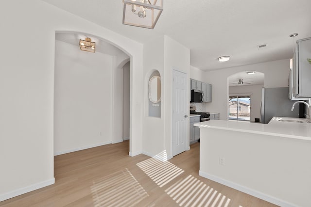 kitchen with a sink, stainless steel appliances, arched walkways, light countertops, and ceiling fan