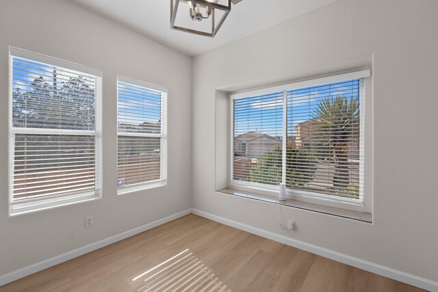 spare room with light wood-style flooring, an inviting chandelier, and baseboards