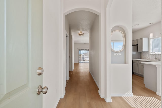 hall with baseboards, arched walkways, a sink, a textured ceiling, and light wood-type flooring