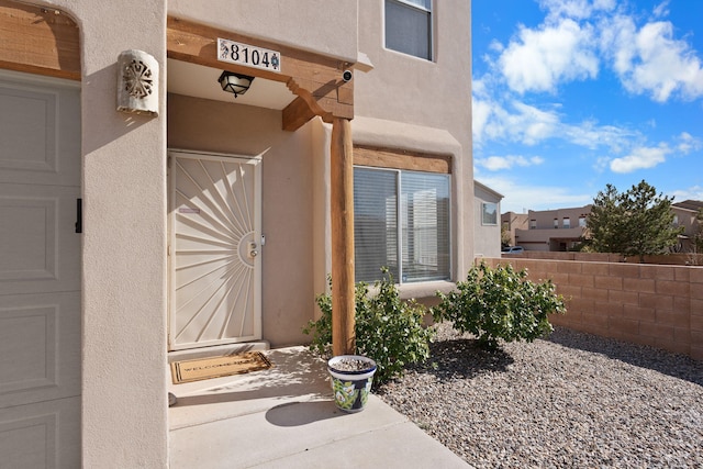 entrance to property with stucco siding, a garage, and fence