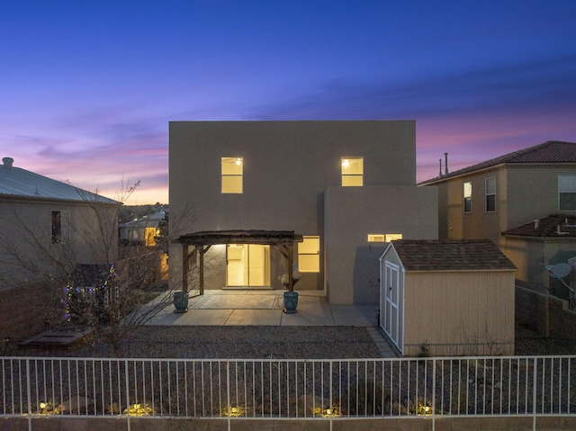 back of house at dusk with an outbuilding, fence, a pergola, stucco siding, and a patio area