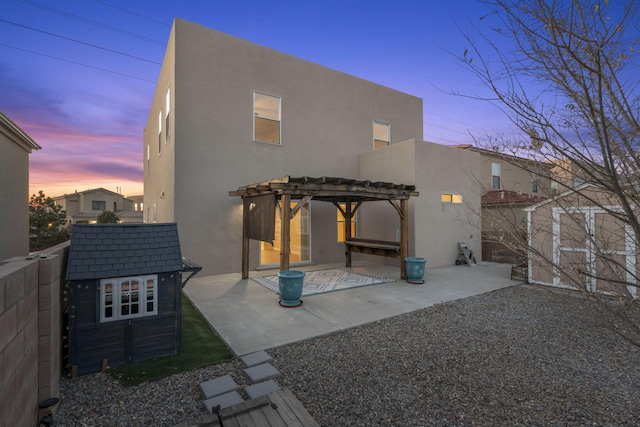 8104 Sleeping Bear Dr NW, Albuquerque, NM 87120 - back of house at dusk with a storage unit, a pergola, stucco siding, and a patio