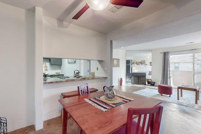 dining space featuring a textured ceiling, concrete floors, a fireplace, visible vents, and a ceiling fan