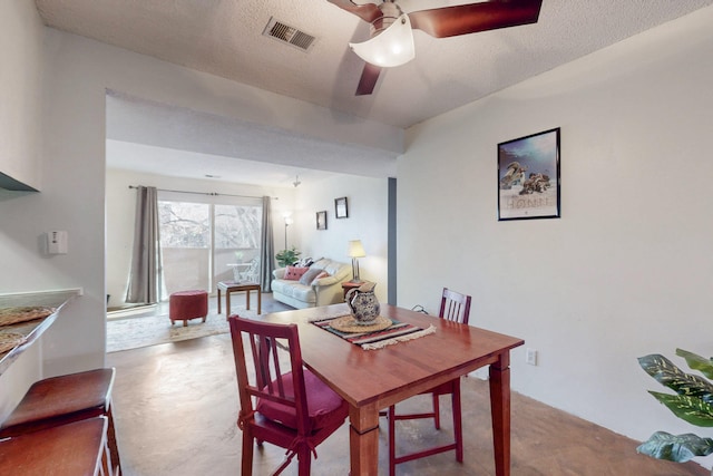 dining area featuring ceiling fan, a textured ceiling, visible vents, and concrete flooring