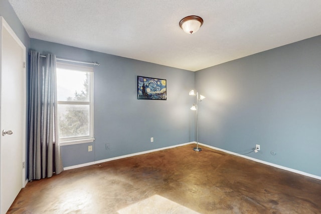 unfurnished room with concrete floors, baseboards, and a textured ceiling