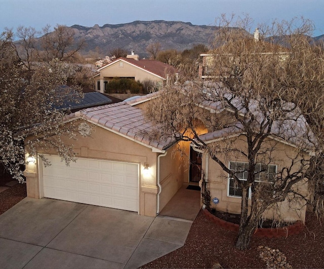 view of front facade featuring concrete driveway, an attached garage, a tile roof, and a mountain view