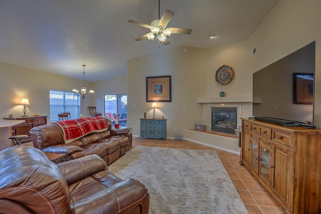 living area with light tile patterned floors, a glass covered fireplace, vaulted ceiling, baseboards, and ceiling fan with notable chandelier