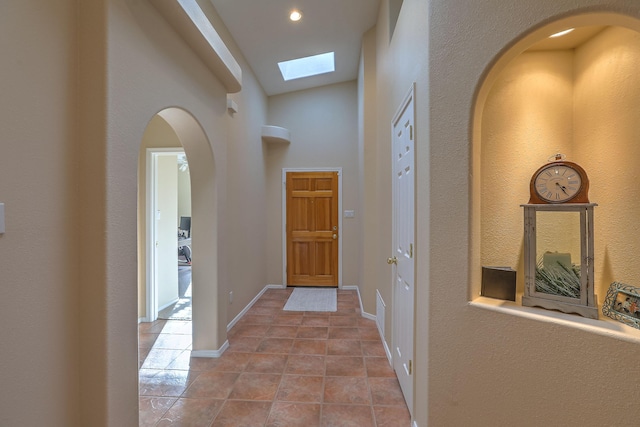 hallway featuring light tile patterned floors, a skylight, baseboards, arched walkways, and a towering ceiling