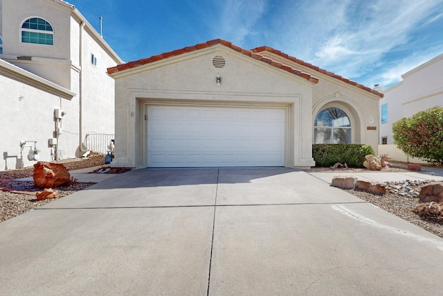 mediterranean / spanish-style home featuring an attached garage, driveway, a tiled roof, and stucco siding