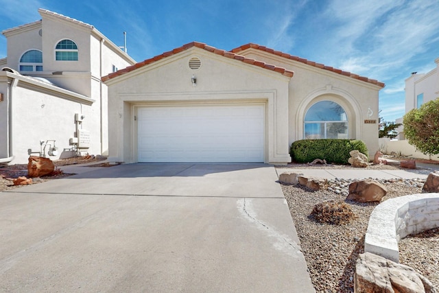 mediterranean / spanish-style home featuring driveway, an attached garage, a tile roof, and stucco siding