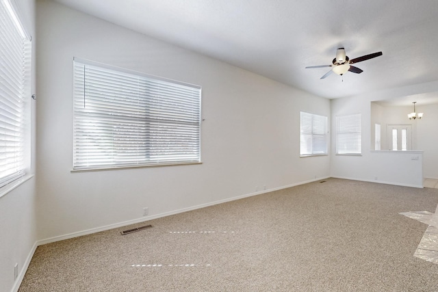 empty room featuring ceiling fan with notable chandelier, light carpet, visible vents, and baseboards