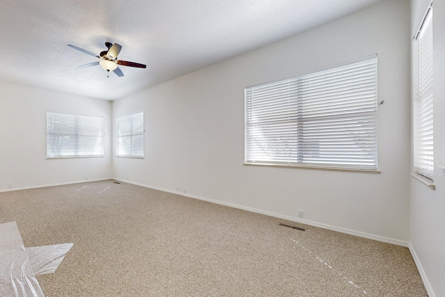 carpeted spare room featuring ceiling fan, visible vents, and baseboards