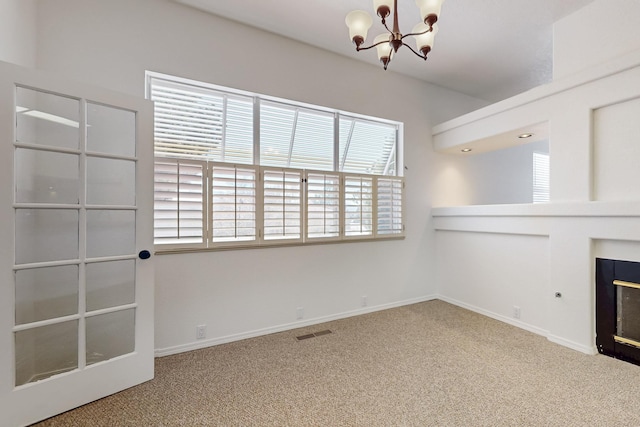 unfurnished living room featuring a notable chandelier, carpet flooring, visible vents, baseboards, and a glass covered fireplace