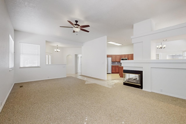 unfurnished living room with ceiling fan with notable chandelier, baseboards, a multi sided fireplace, and light colored carpet