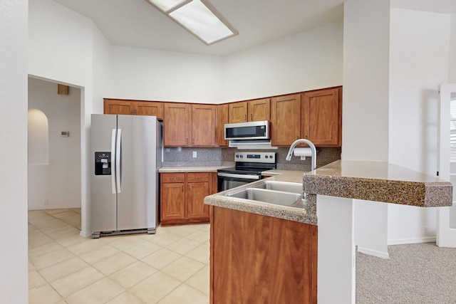 kitchen featuring high vaulted ceiling, stainless steel appliances, a sink, backsplash, and brown cabinetry