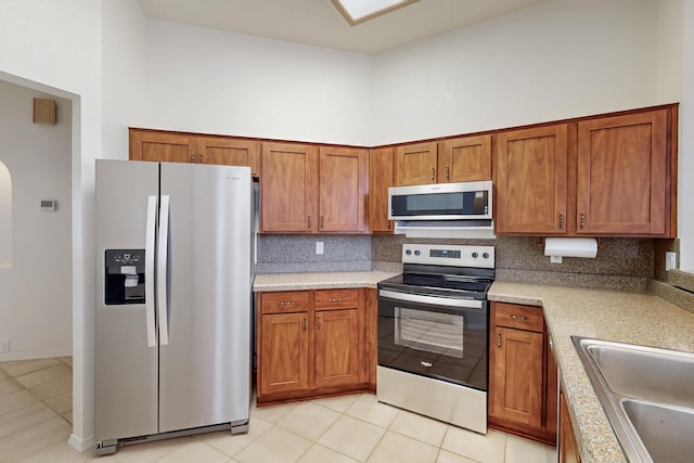 kitchen featuring light countertops, decorative backsplash, appliances with stainless steel finishes, brown cabinetry, and a sink