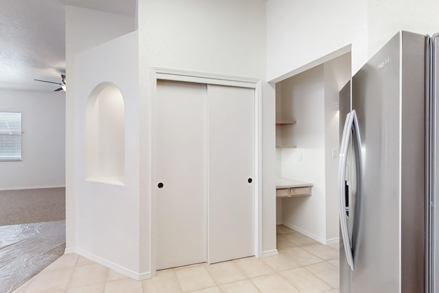 interior space featuring a ceiling fan, freestanding refrigerator, baseboards, and light tile patterned floors