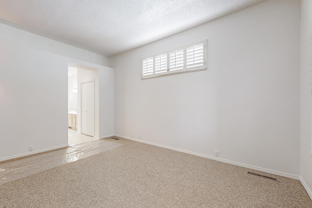 unfurnished room with visible vents, light colored carpet, a textured ceiling, and baseboards