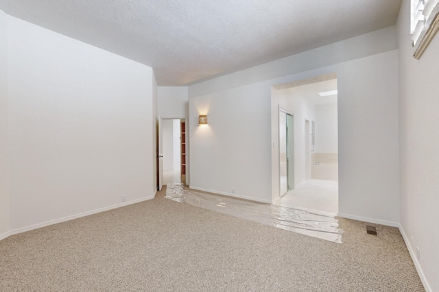 spare room featuring visible vents, light carpet, a textured ceiling, and baseboards