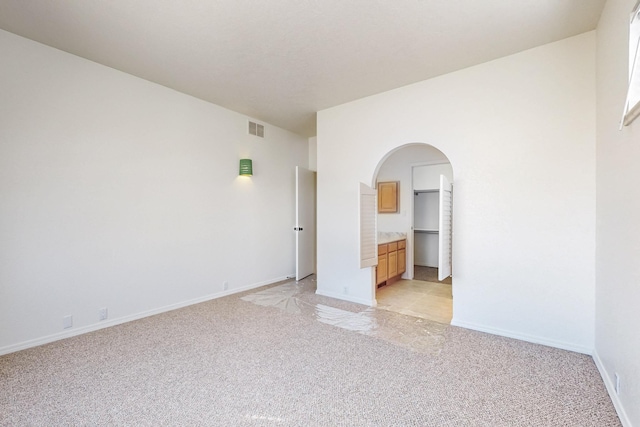 spare room with light carpet, arched walkways, visible vents, and baseboards