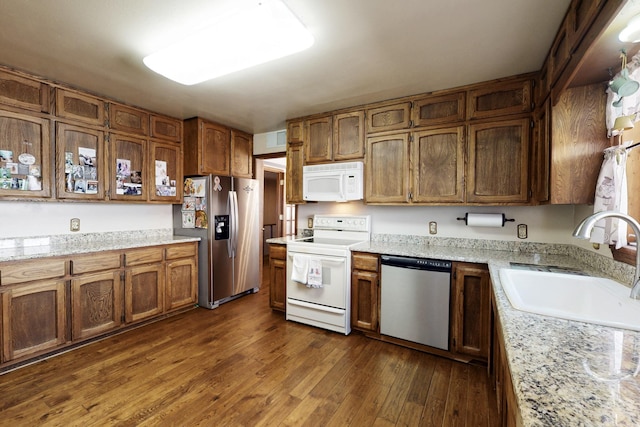 kitchen featuring appliances with stainless steel finishes, brown cabinets, dark wood-style flooring, light stone countertops, and a sink