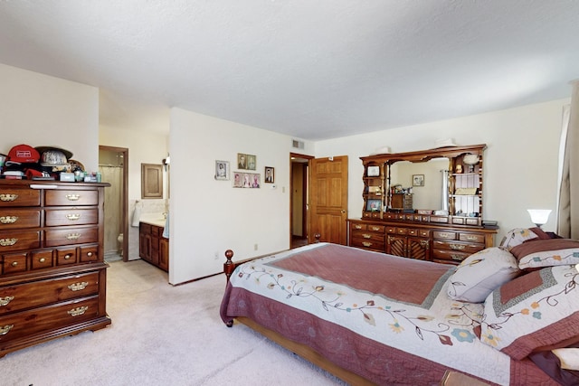 bedroom with baseboards, ensuite bath, visible vents, and light colored carpet