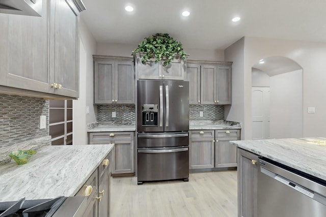 kitchen with tasteful backsplash, arched walkways, appliances with stainless steel finishes, light stone counters, and light wood-type flooring