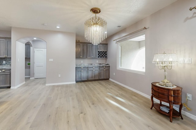 kitchen with arched walkways, a notable chandelier, light countertops, light wood-type flooring, and baseboards