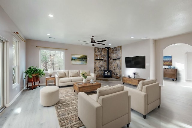 living area featuring arched walkways, recessed lighting, visible vents, light wood-style floors, and a wood stove