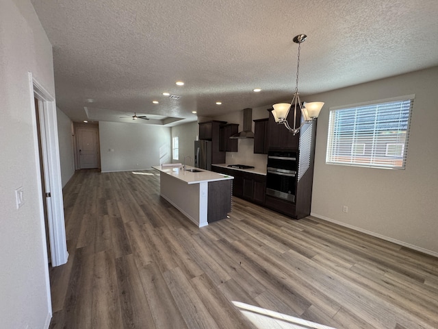 kitchen featuring stainless steel appliances, a textured ceiling, open floor plan, and wall chimney range hood