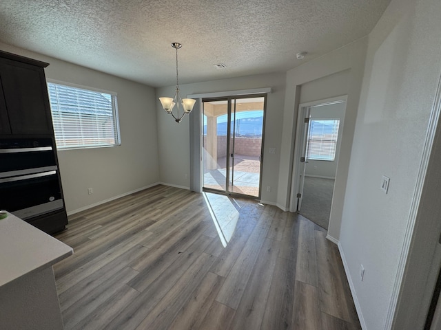 unfurnished dining area featuring an inviting chandelier, a textured ceiling, light wood finished floors, and baseboards