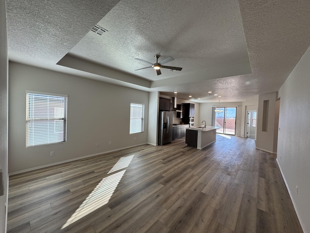 unfurnished living room with plenty of natural light, a textured ceiling, a ceiling fan, and a tray ceiling