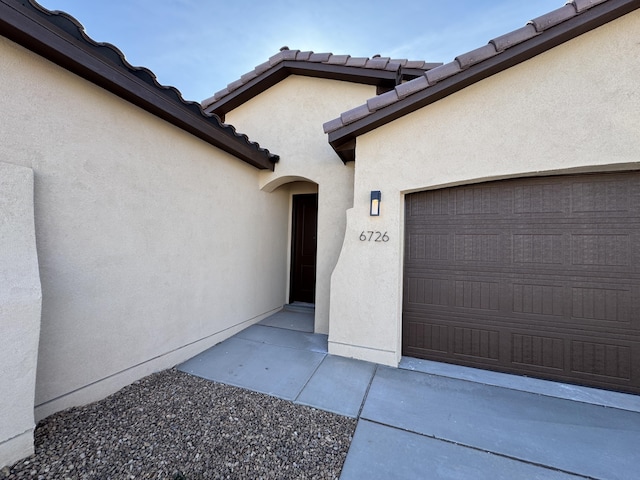doorway to property featuring stucco siding, a tiled roof, and a garage