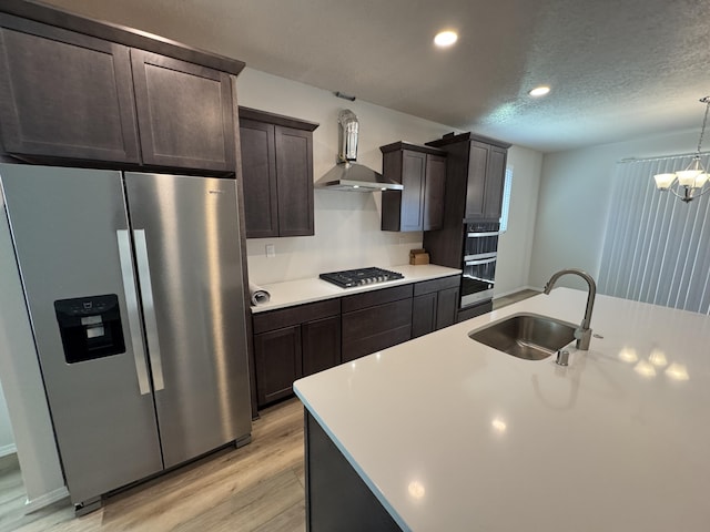 kitchen with wall chimney range hood, light wood-style flooring, a sink, appliances with stainless steel finishes, and light countertops