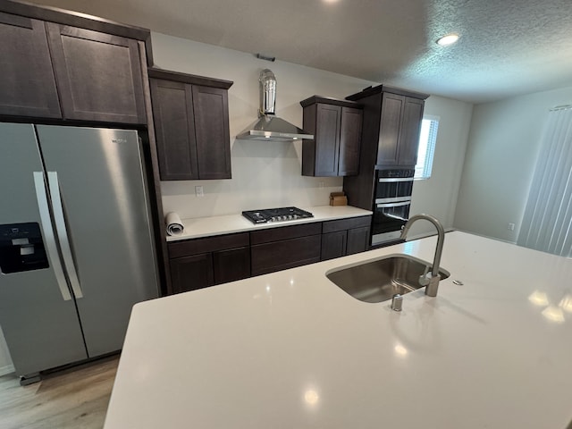 kitchen with stainless steel appliances, light countertops, wall chimney range hood, a sink, and a textured ceiling