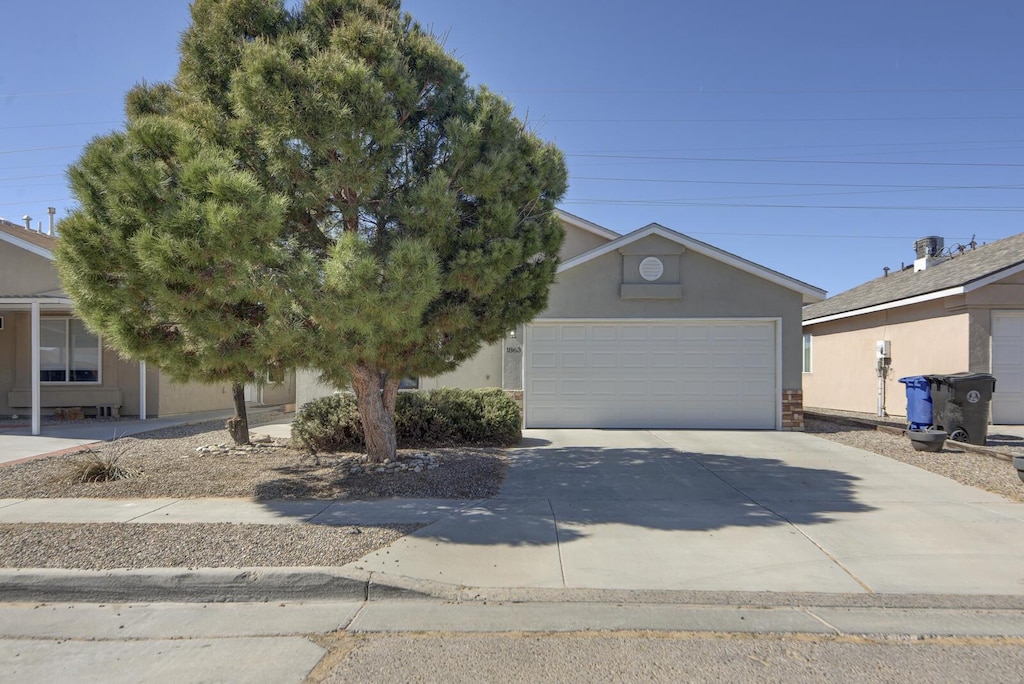 obstructed view of property featuring a garage, stone siding, driveway, and stucco siding