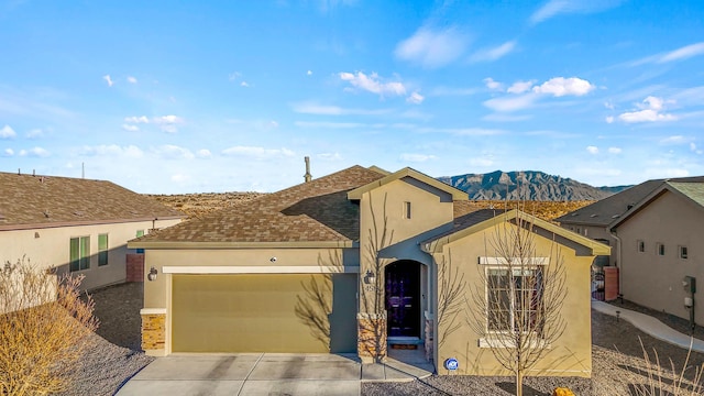 view of front of home with stucco siding, driveway, a mountain view, roof with shingles, and a garage