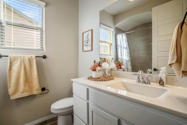 bathroom featuring vanity, toilet, baseboards, and a tile shower