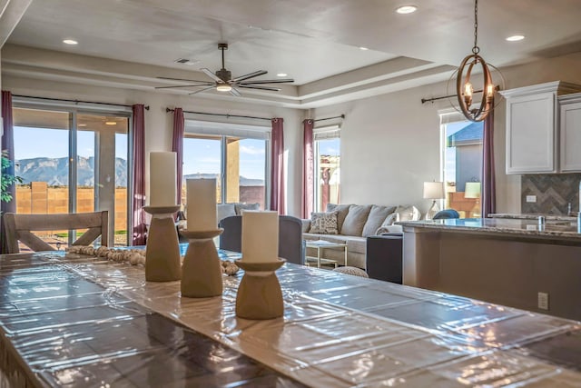 dining room with recessed lighting, a mountain view, a raised ceiling, and ceiling fan with notable chandelier