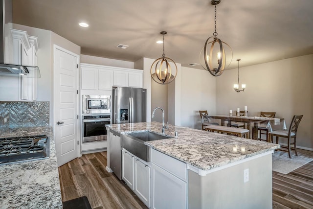 kitchen featuring decorative backsplash, dark wood-style flooring, stainless steel appliances, wall chimney exhaust hood, and a sink