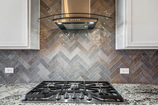 room details featuring white cabinetry, stainless steel gas stovetop, light stone countertops, and backsplash